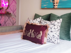 A bed with a purple pillow featuring a leopard print design, surrounded by green and white patterned pillows.