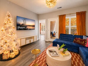 A living room with a white Christmas tree, a blue sofa, a round coffee table, and a television displaying a scenic image.