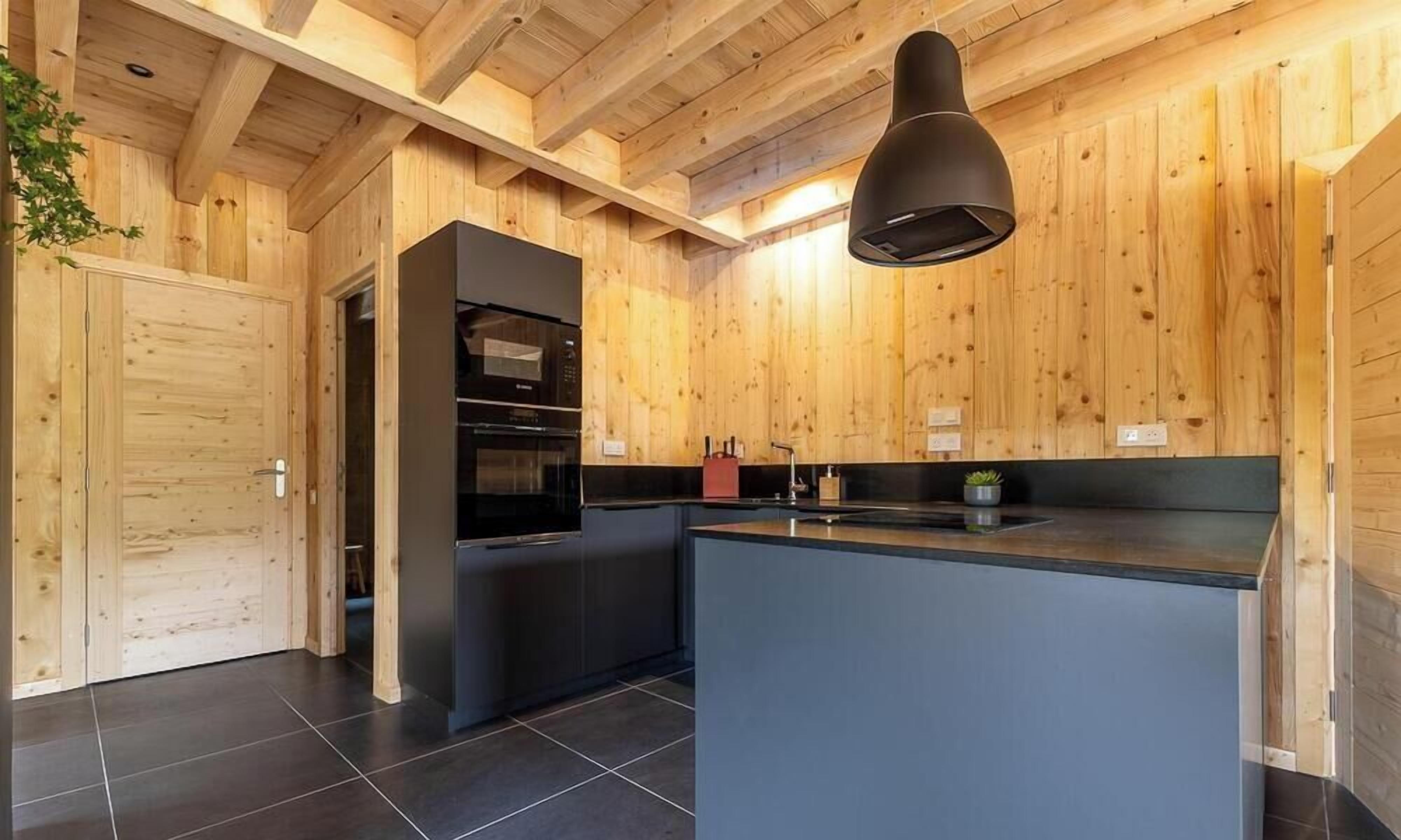 Una cocina moderna con paredes de madera, un refrigerador negro y una isla central.