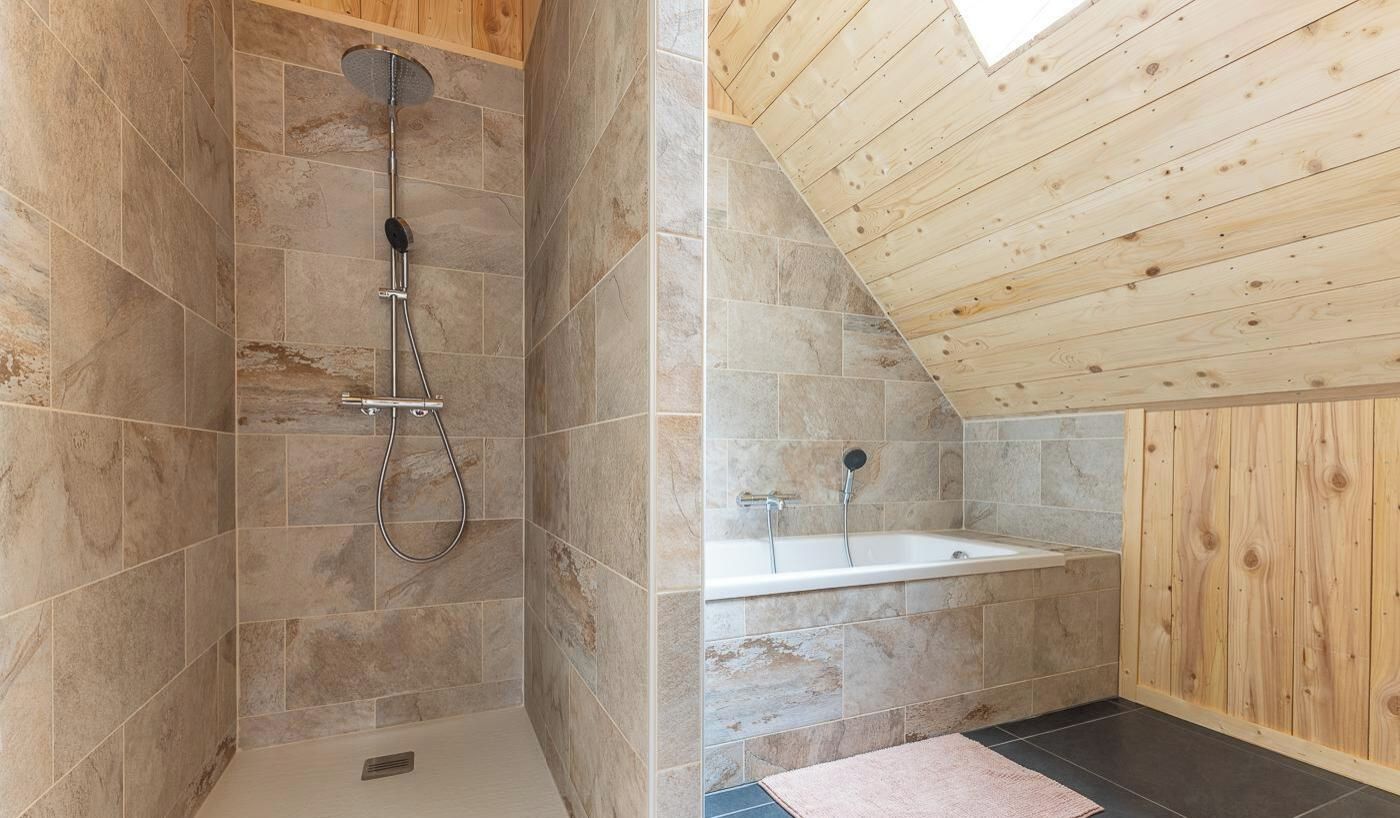 A bathroom with a shower, a bathtub, and wooden ceiling beams.
