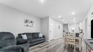 A modern living room with a grey sofa, a dining area with a wooden table and chairs, and a kitchen in the background. - No Steps! Peaceful, Picturesque & Quiet Location - 3 Bed 2 Bath Condo (Branson)