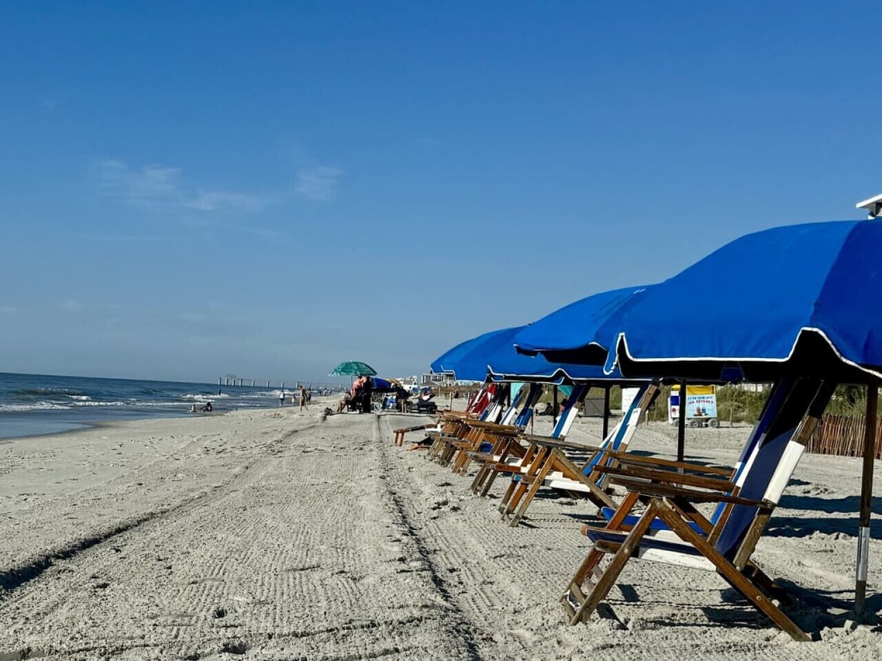 Una platja amb files de papereres blaves i cadiretes de fusta.
