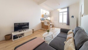 Ein modernes Wohnzimmer mit Flachbildfernseher, Sofa und einer kleinen Essecke mit Tisch und Stühlen.