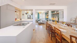 A modern kitchen with a central island, wooden dining table, and chairs. There is a view into the dining area with a sofa and a kitchen counter. - Là-Haut - Rooftop - Panorama sur la ville Parking (Montpellier)