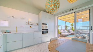 A modern kitchen with white cabinets, a wooden dining table, and a view of an outdoor patio with seating. - Là-Haut - Rooftop - Panorama sur la ville Parking (Montpellier)