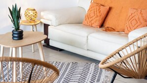 Una sala de estar moderna con un sofá blanco, almohadones naranjas, una mesita redonda con una planta y una lámpara decorativa.
