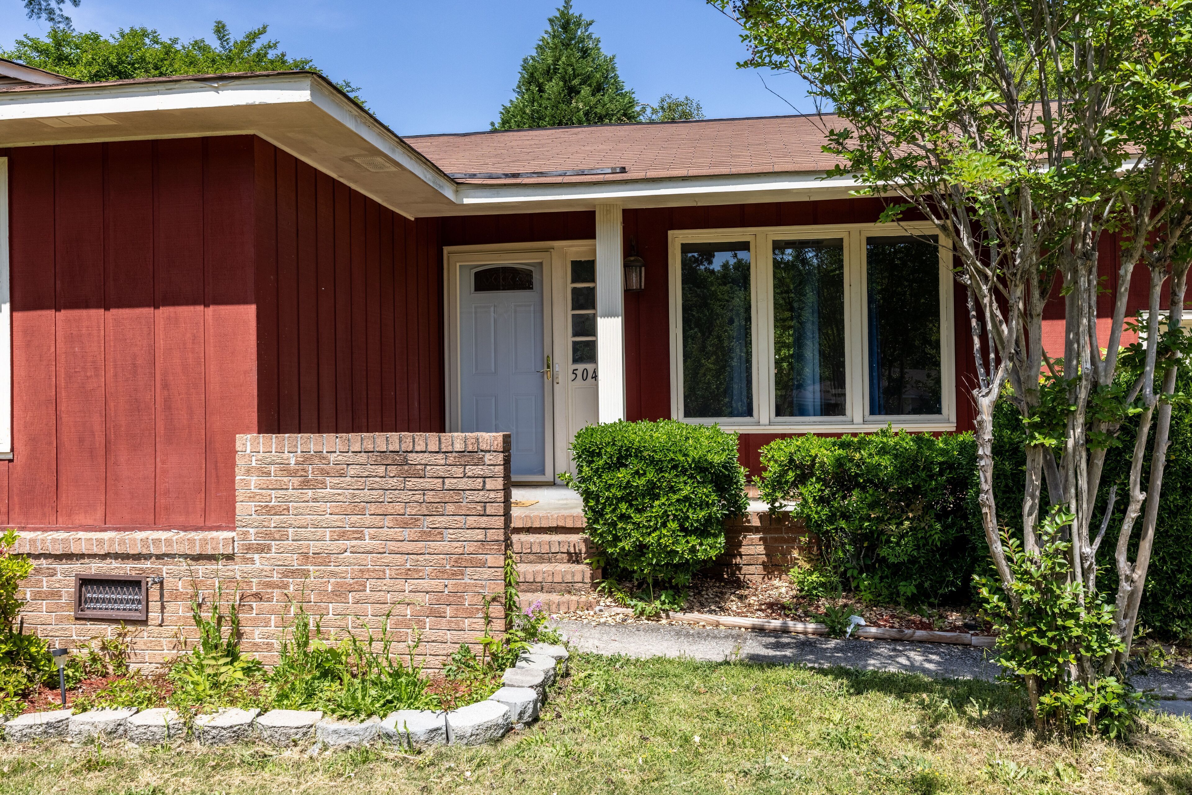 Une maison de plain-pied à l’extérieur rouge, avec une porte blanche et des fondations en briques.