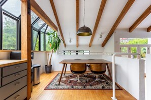 A modern kitchen with wooden beams, a large window, a dining table with chairs, and a potted plant.