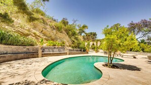 Ein Pool mit geschwungener Form, umgeben von einer Steindeck und einer Grünanlage mit Bäumen und Pflanzen.