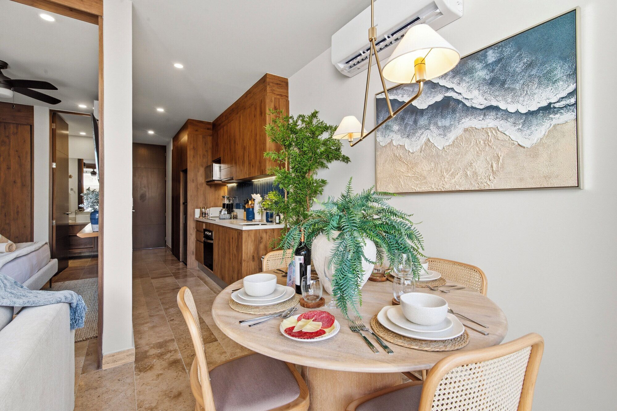 Un coin repas avec une table ronde, des chaises et un tableau représentant une scène de plage.