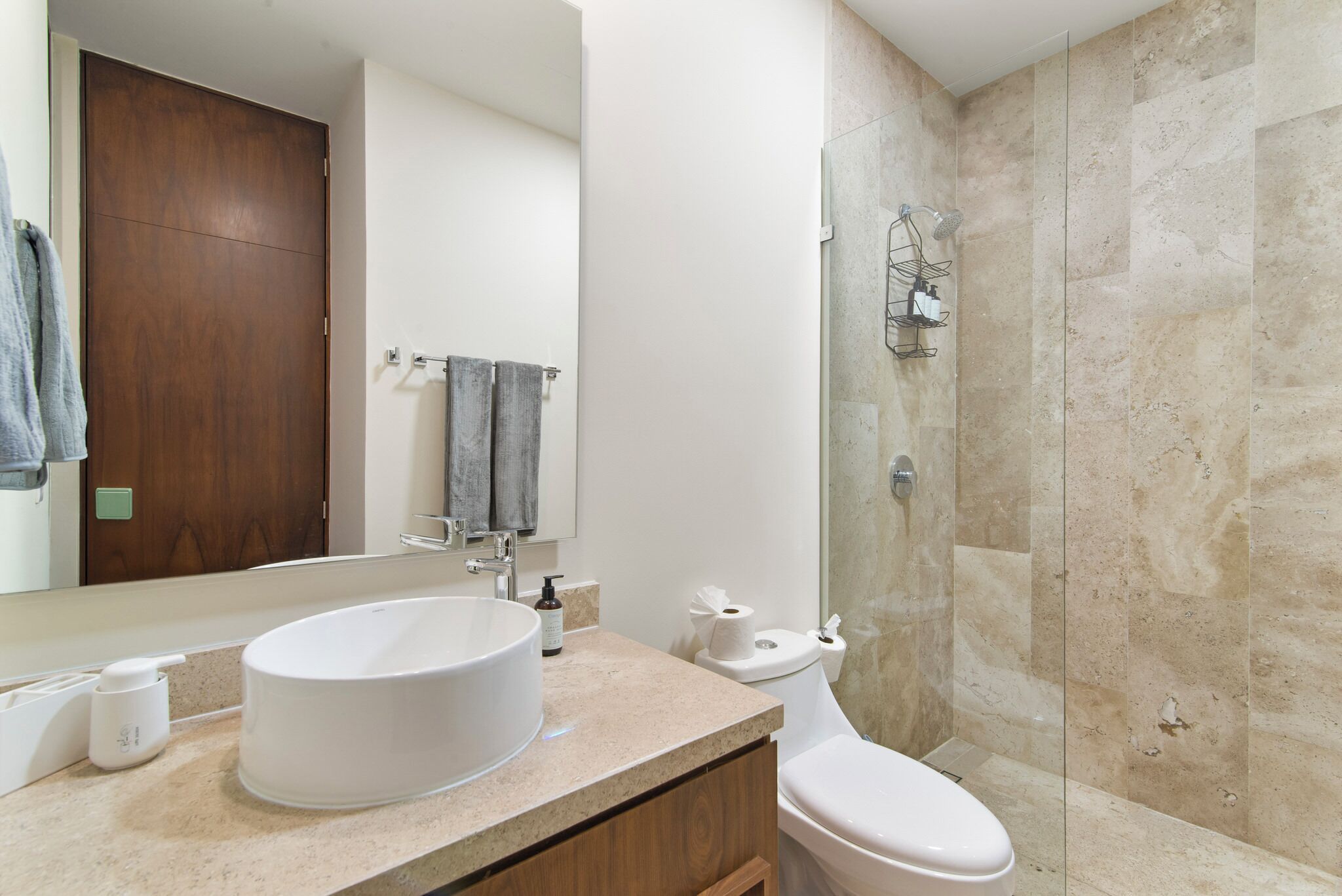 A bathroom with a round sink, a toilet, a shower with a glass door, and a wooden door in the background.