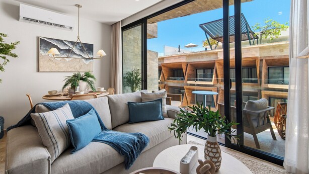 Een moderne woonkamer met een bank, een bijzettafeltje en uitzicht op een terras met houten meubels.