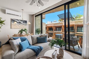 Ein modernes Wohnzimmer mit einer Couch, einem Couchtisch und Blick auf eine Außen-Terrasse mit Holzmöbeln.