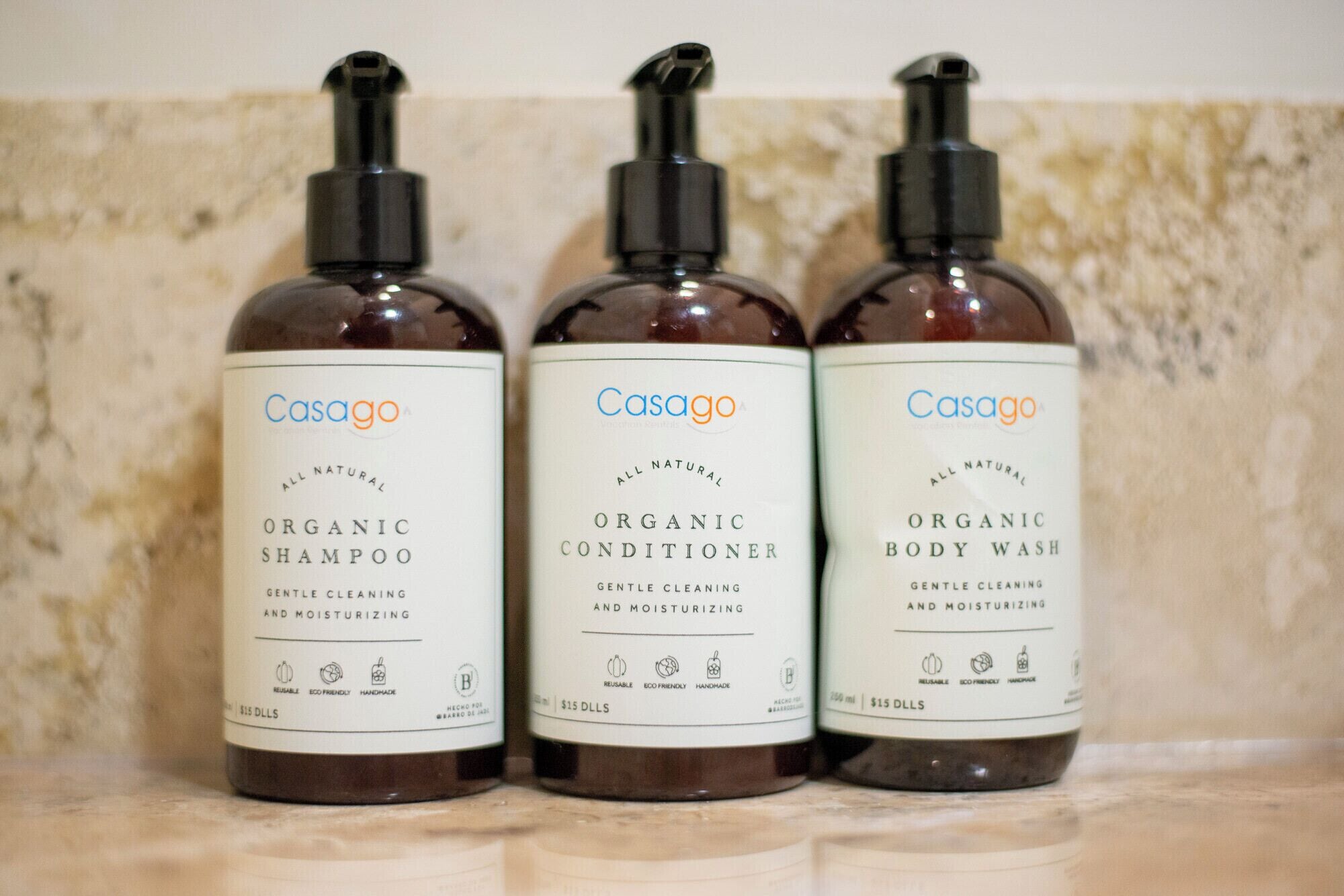 Drei Flaschen Casago Bio-Shampoo, -Spülung und -Duschgel auf einer Marmorplatte.