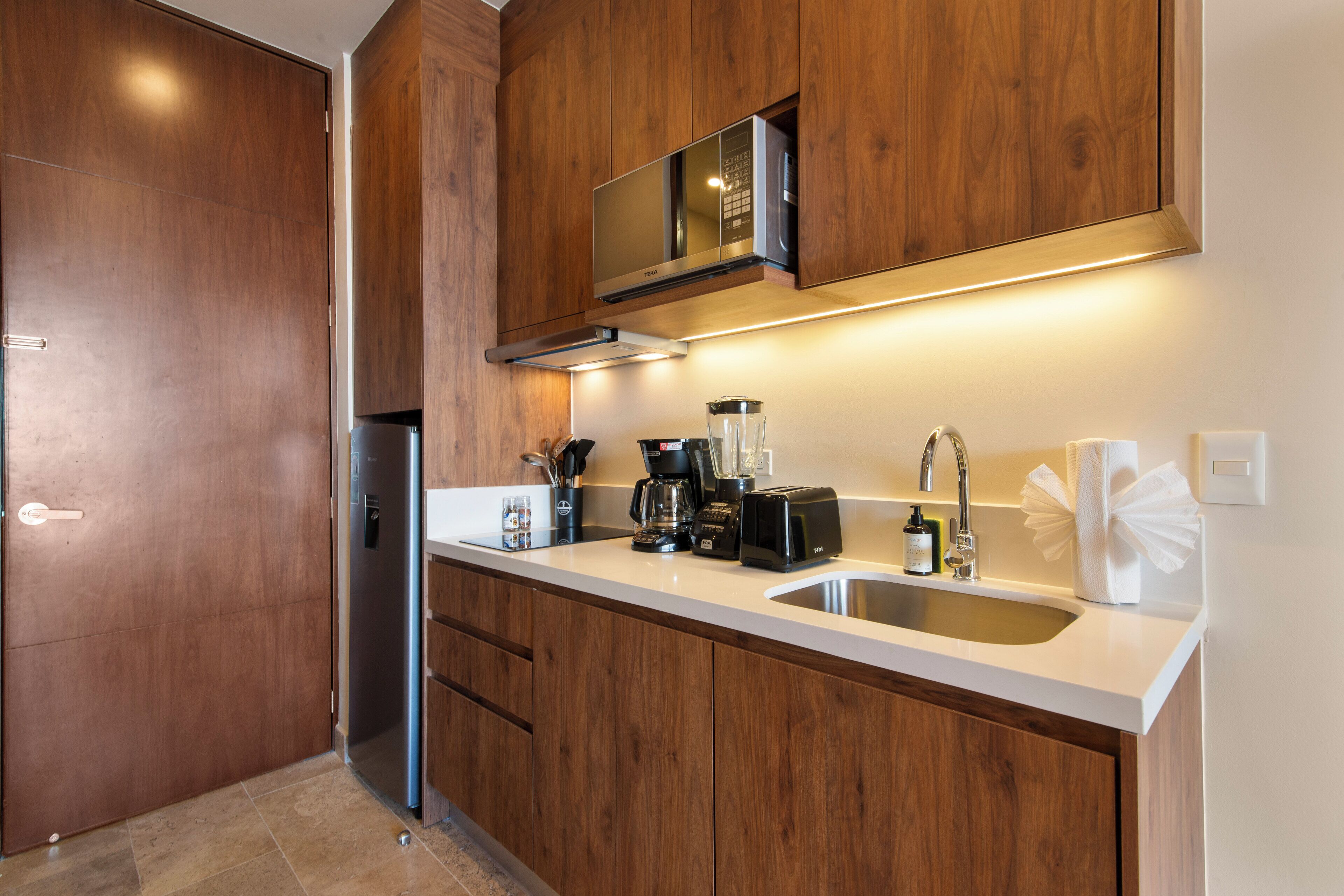 Una cocina moderna con armarios de madera, un refrigerador de acero inoxidable, un microondas, una cafetera y un fregadero.