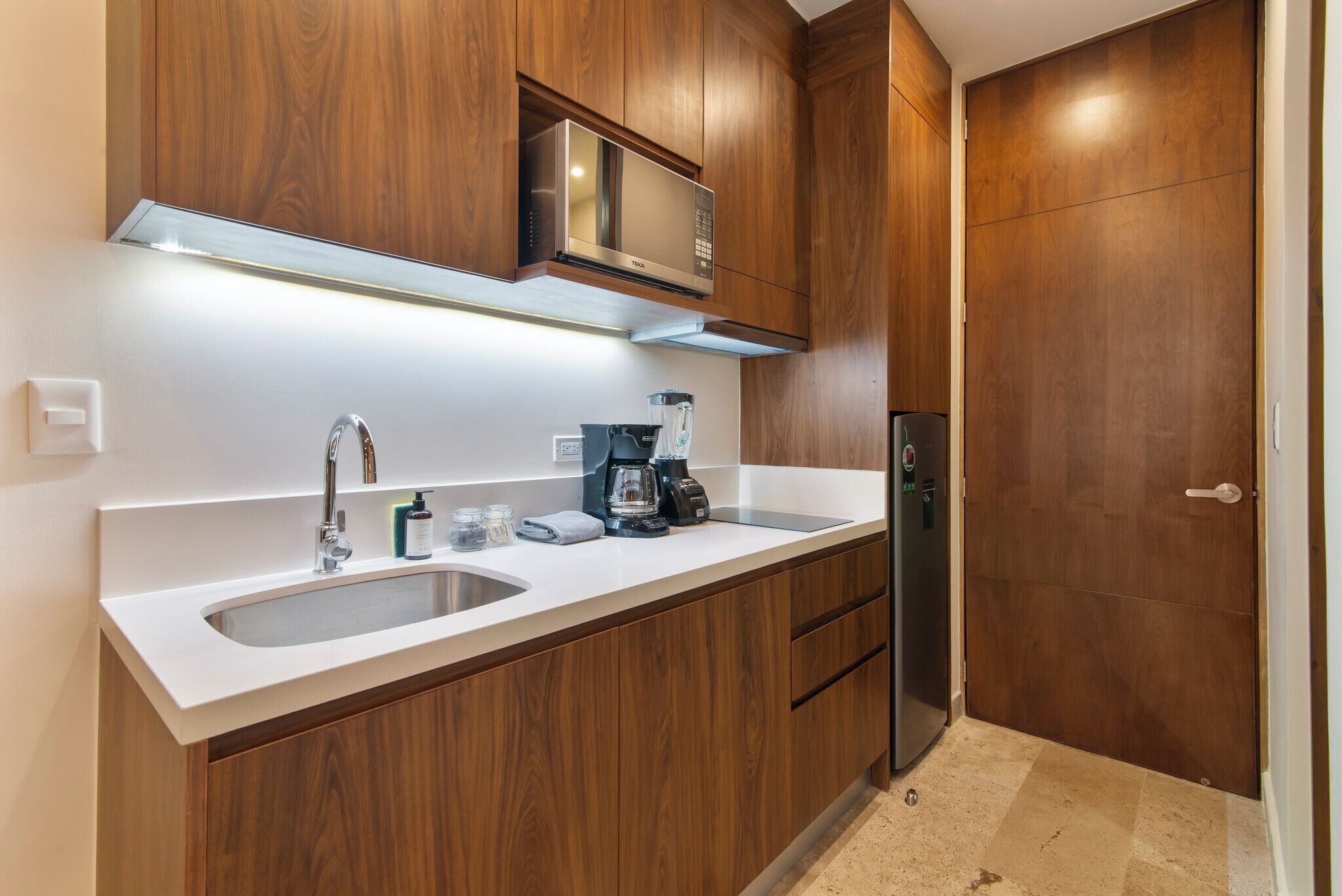 A modern kitchen with wooden cabinets, a stainless steel microwave, a coffee maker, and a refrigerator.