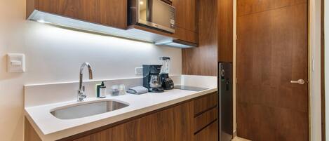A modern kitchen with wooden cabinets, a stainless steel microwave, a coffee maker, and a refrigerator.