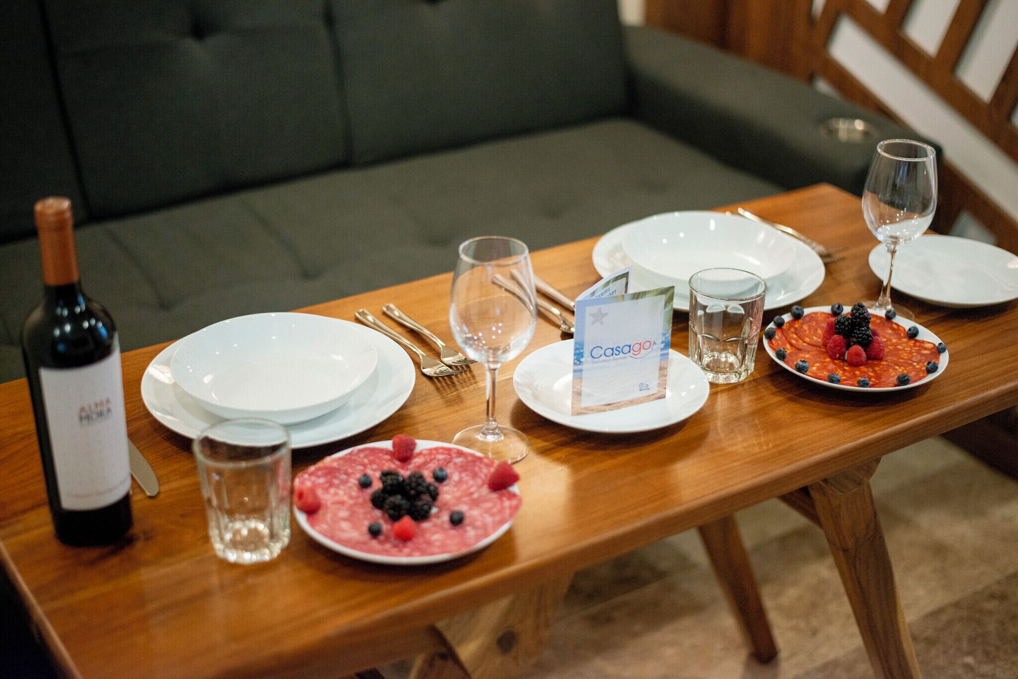 A dining table set with plates, cutlery, glasses, and a bottle of wine.