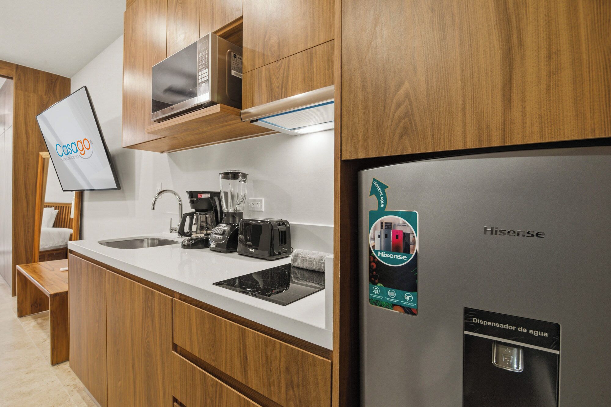 A modern kitchen with wooden cabinets, a stainless steel refrigerator, a coffee maker, a toaster, and a sink.