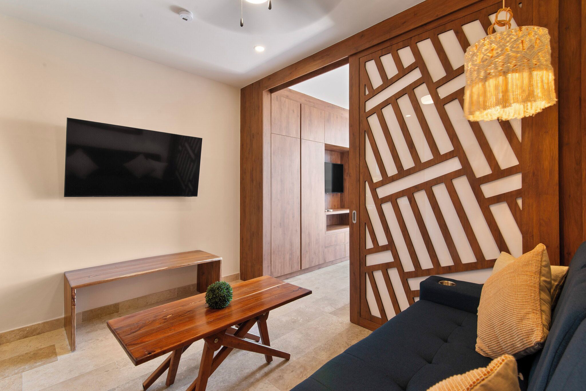Una sala de estar moderna con un separador de madera, un televisor montado en la pared, un sofá, un banco y una lámpara colgante.