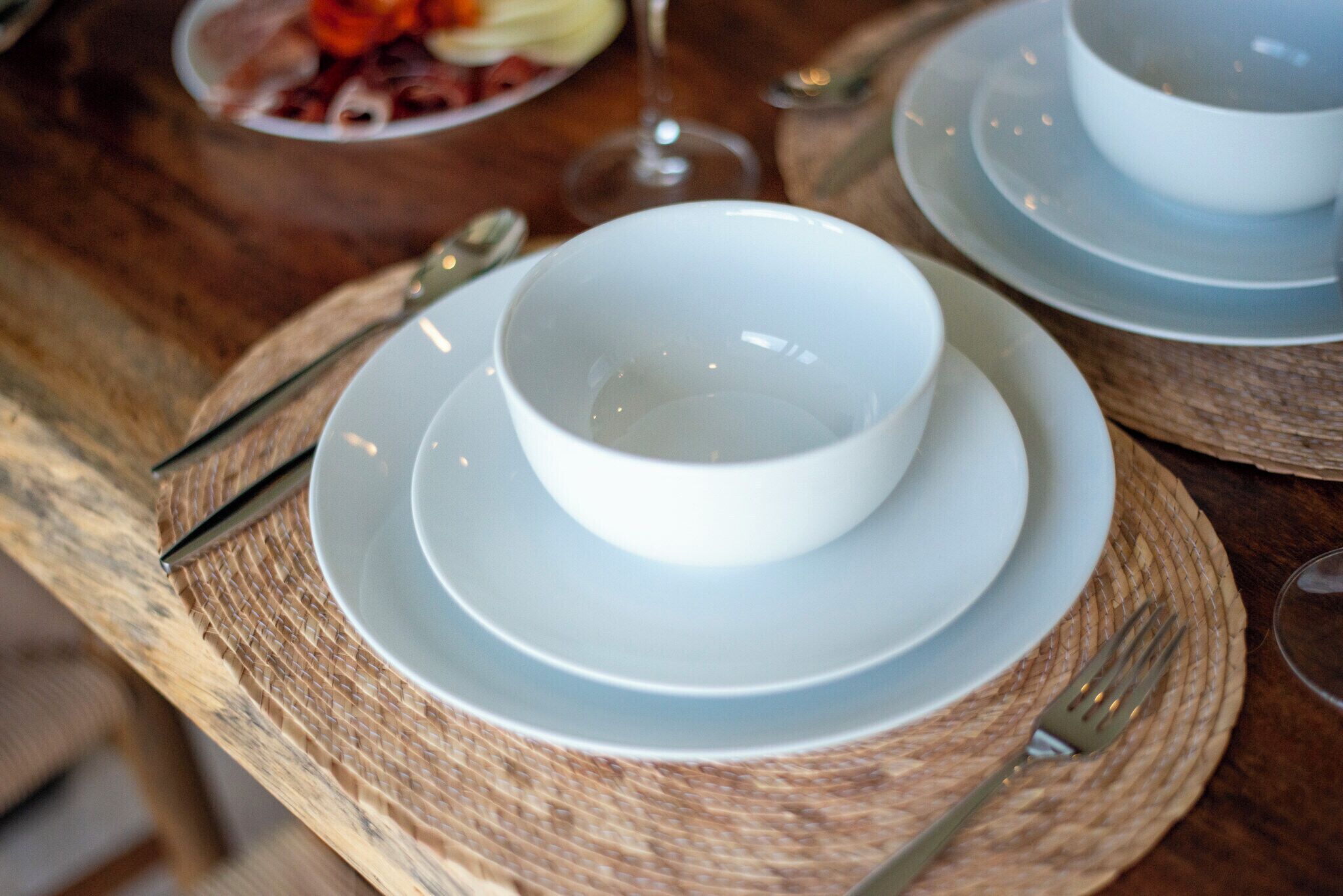 Een eettafel met een witte kom op een bord, een vork en een glas water.
