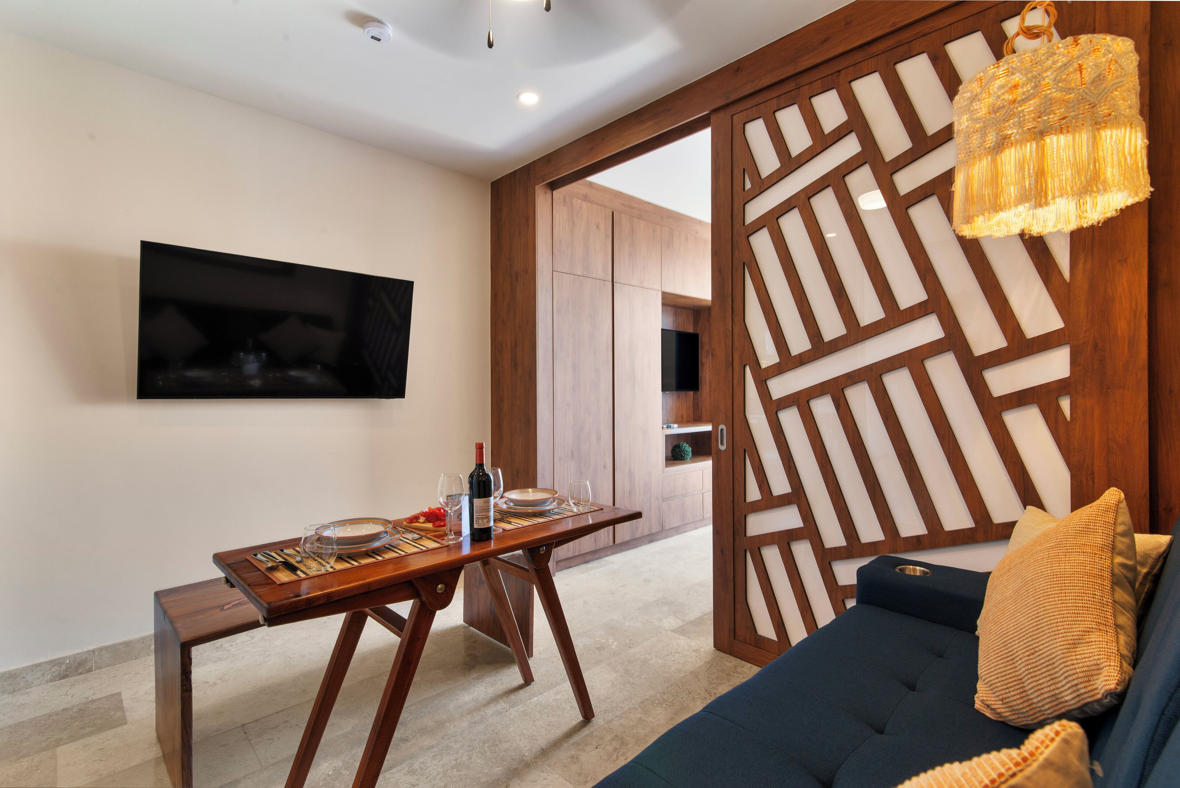 Una sala de estar moderna con un sofá azul oscuro, una mesa de comedor de madera y un televisor montado en la pared.