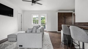 A modern living room with a sofa, a ceiling fan, and a large window. - 1 Bedroom Anchor Cottage 2 - One bedroom, one murphy bed, one sleeper sofa, with kitchenette (Allons)