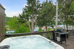 Een hottub op een houten terras met uitzicht op een jachthaven en bomen.