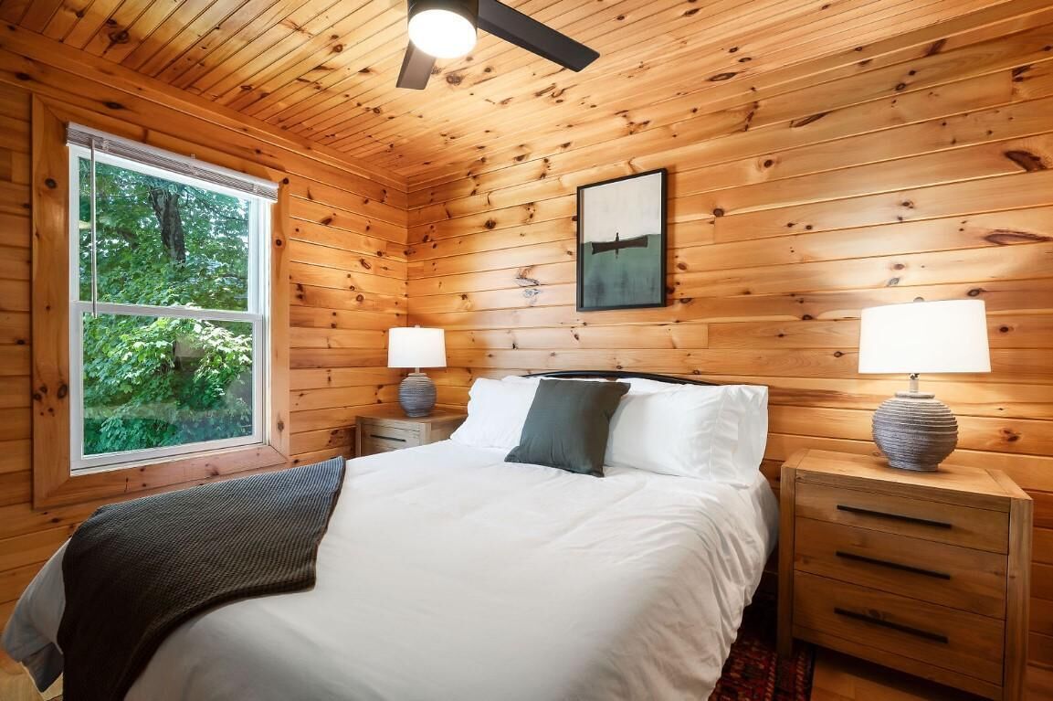 A wooden cabin bedroom with a bed, two bedside tables, a window, and a ceiling fan.