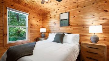 A wooden cabin bedroom with a bed, two bedside tables, a window, and a ceiling fan.