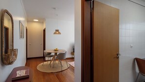 Una habitación moderna con puerta de madera, una mesa redonda con sillas, una lámpara colgante y un espejo en la pared.
