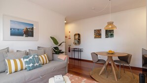 Una sala de estar moderna con un sofá gris, una mesita redonda y un comedor con sillas.