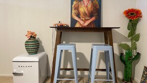Una kitchenette compacta con un refrigerador blanco Galanz, un pequeño coche de juguete naranja y un cuadro enmarcado sobre una mesa de madera con dos taburetes azul claro.
