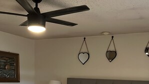 Un dormitorio con cama, mesitas de noche, ventilador de techo y adornos en forma de corazón en la pared.
