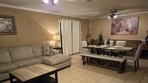 Una sala de estar con un sofá modular, una mesa de centro, una mesa de comedor con sillas, un pequeño árbol de Navidad y un cuadro en la pared.