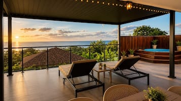 Un'area esterna coperta con piscina, lettini e vista sull'oceano al tramonto.