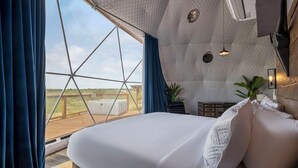 Une pièce spacieuse dotée d’un grand lit, offrant une vue sur l’extérieur et présentant un plafond au design géométrique original.