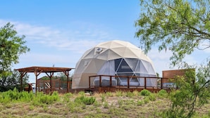 Une structure en forme de dôme géodésique dotée d’une terrasse en bois et d’un espace abrité.
