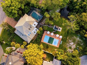Vista aérea de una propiedad residencial con piscina, cancha de tenis y zona de patio con sombrillas.