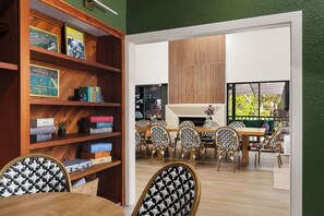 A room with a wooden bookshelf, a dining table with chairs, and a view through a glass door.