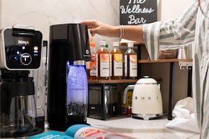 Una cucina con una macchina per il caffè, un dispenser d'acqua e una moka. Sul bancone ci sono bottiglie di bevande.