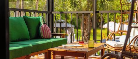 A wooden deck with a green sofa, a wicker chair, and a table with a glass of red wine and a yellow candle.