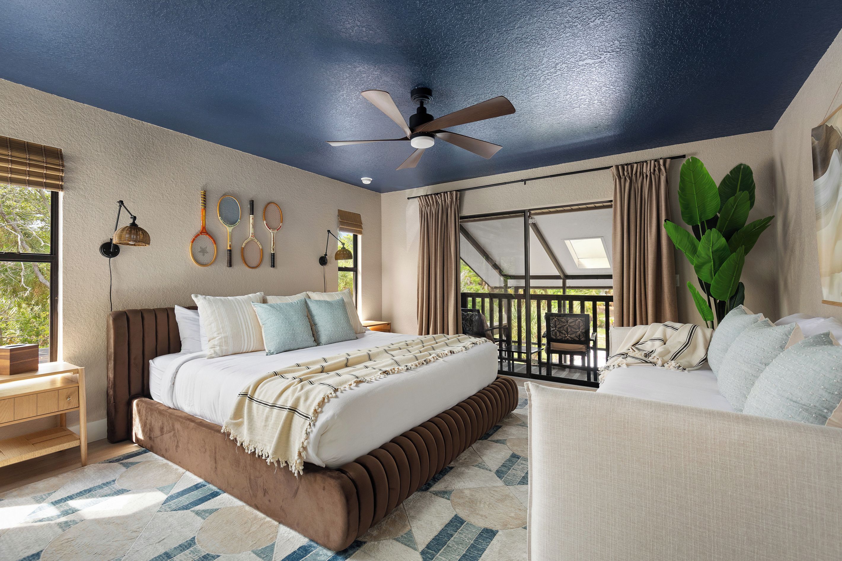A bedroom with a bed, a sofa, a ceiling fan, and a view of the outdoors.