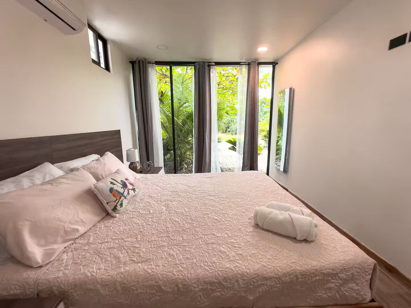 Un dormitorio con una cama grande, una mesita de noche, una ventana con cortinas y vistas al exterior.