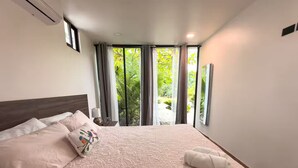 Un dormitorio con una cama grande, una mesita de noche, una ventana con cortinas y vistas al exterior.