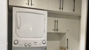 Cocina compacta con lavadora y secadora de carga frontal, armarios blancos y un lavamanos pequeño.