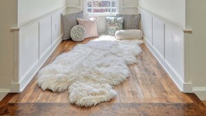 Une chambre mansardée chaleureuse avec un plafond en pente, une fenêtre offrant une belle vue, un tapis blanc moelleux et un lit agrémenté d’oreillers à motifs.