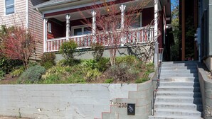 A two-story house with a front porch, a stone retaining wall, and a set of concrete stairs leading to the entrance. - 3BR/2BA • Patio • Steps to Mississippi Ave (Portland)