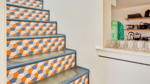 A staircase with a geometric patterned design, leading to a kitchen area with shelves and kitchenware. - 3BR/2BA • Patio • Steps to Mississippi Ave (Portland)