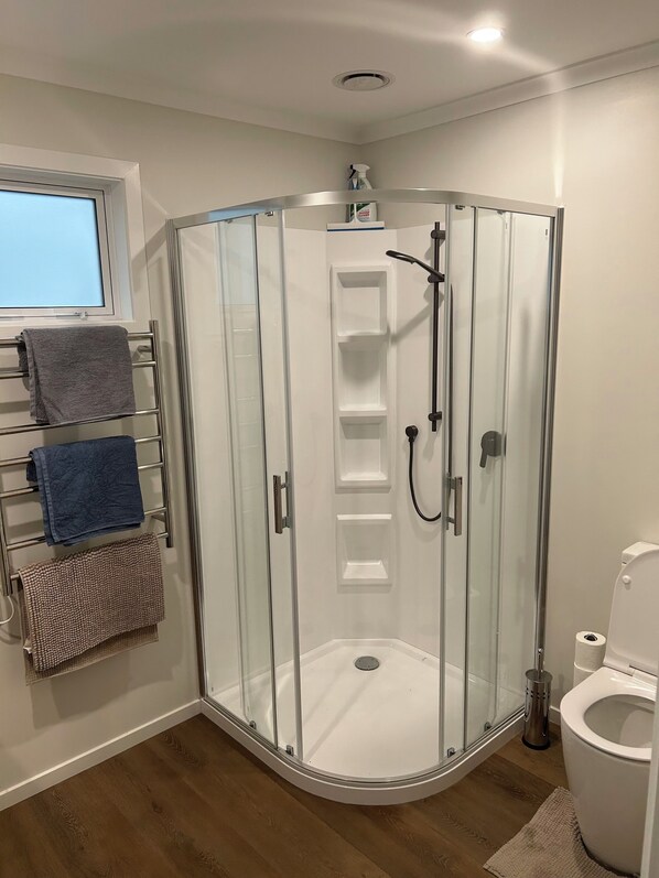A modern bathroom with a glass-enclosed shower, a toilet, and a towel rack with multiple towels.
